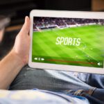 Man watching sports on tablet. Football and soccer game live stream and video player on screen. Pay per view (PPV) service. Replay or highlights broadcast. Lazy person relaxing.